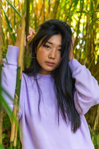 A vertical shot of a beautiful Chinese girl's portrait, posing near bamboo plants, outdoors during daylight