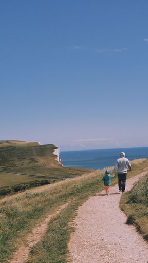 A vertical shot of a male and a kid walking a footpath leading into the Beachy Head cliff and its lighthouse in Sussex, England