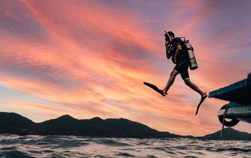 A scuba diver jumping from a boat into the sea at sunset in Koh Tao, Thailand.