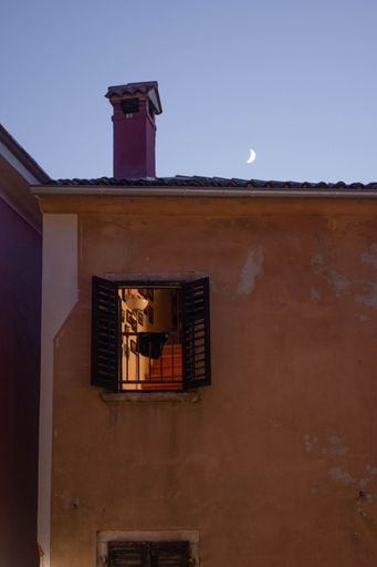 A vertical shot of an open window in an old orange building at night with the Mood in the background