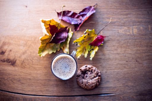 A selective focus shot of a hot autumn drink with a cookie on the side on a wooden surface