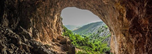 The lush green vegetation of a mountain seen through the opening of Peshna Cave in Macedonia