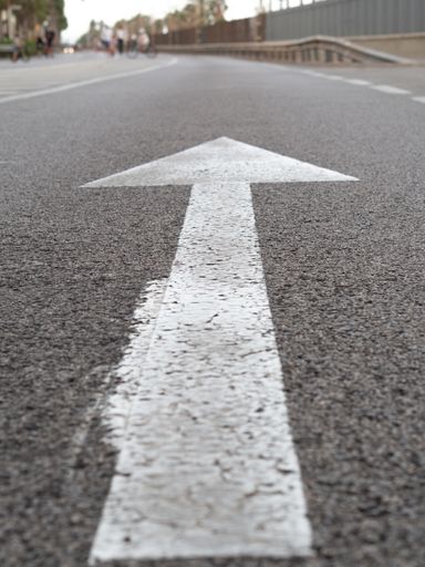 A vertical closeup shot of a white arrow on asphalt of a road traffic signal
