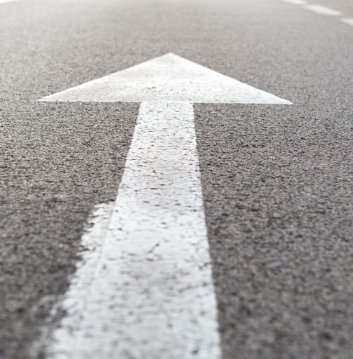 A vertical closeup shot of a white arrow on asphalt of a road traffic signal