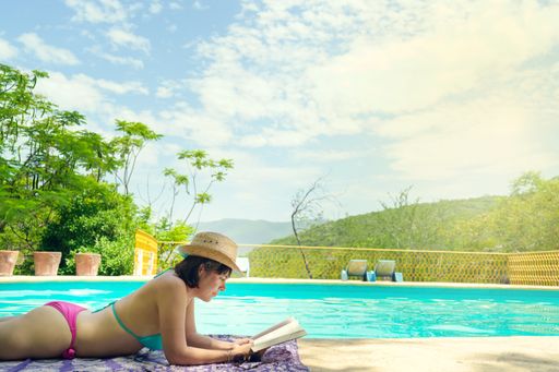 A young woman sunbathing with a book lying near a swimming pool