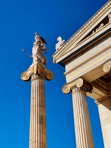 A vertical low angle shot of a statue by the entrance of Academy of Athens university in Athens, Greece