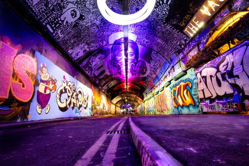 A long tunnel with vibrant graffiti covering its walls illuminated by purple led lights