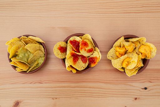 A top view of three plates of nachos with sauce