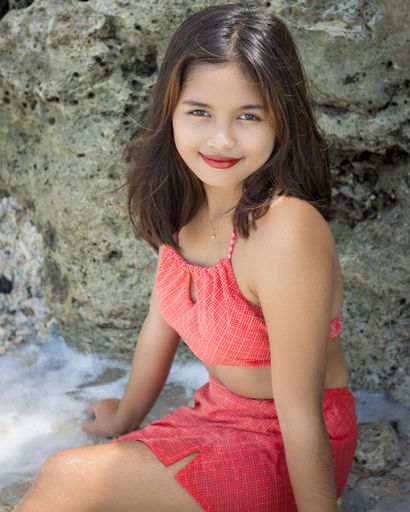 A beautiful Filipina in a red swimsuit smiling and posing at a beach with a rock in the background