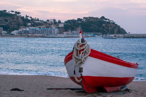 White boat moored to the sand of the beach of the town of Blanes with the beautiful colors of a sunset in background.