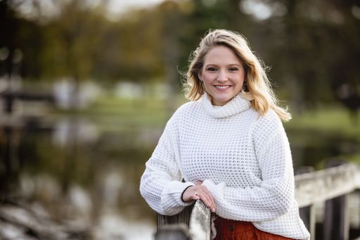 A shallow focus shot of a female leaning against a wooden fence and smiling at the camera