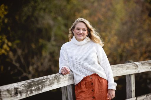 A shallow focus shot of a female leaning against a wooden fence and smiling at the camera
