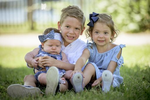 A shallow focus shot of children with their newborn sister sitting on the grass