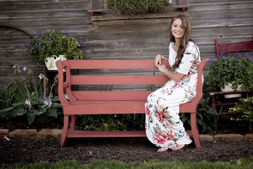 A beautiful shot of a female sitting on a wooden bench while smiling at the camera