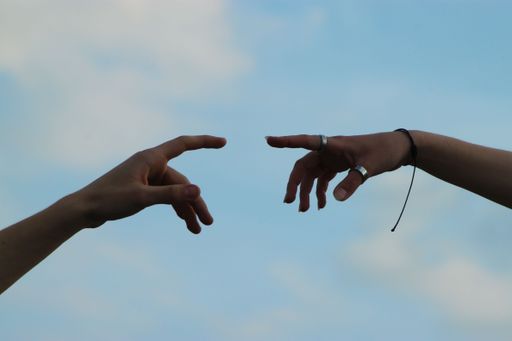 A closeup shot of a couple reaching fingers to touch hands isolated on the background of the sky