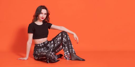 Cheerful young brunette girl in black and white trouser casual suit sits on orange background and looks into camera.