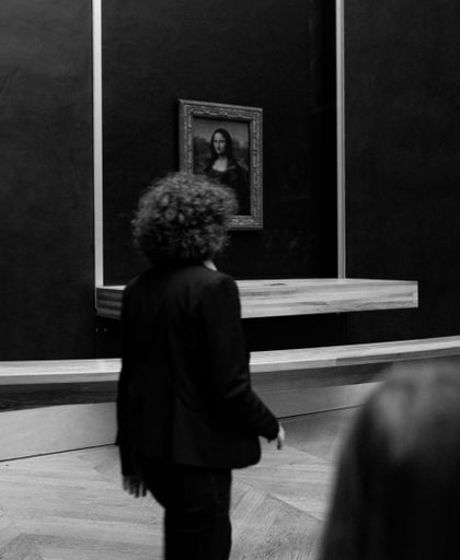 A vertical grayscale shot of a person near the Mona Lisa in Louvre, Paris, France