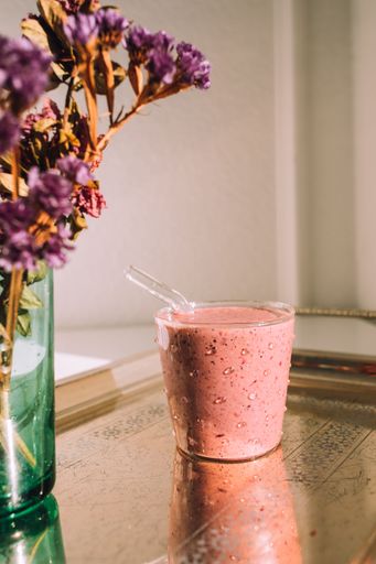 pink mixed berry smoothie with glass straw on silver tray with dried flowers in green glass vase