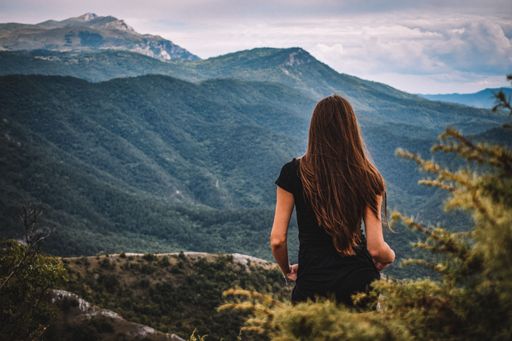 A back view of a female with long dark hair standing on highlands, with grass mountains in the background