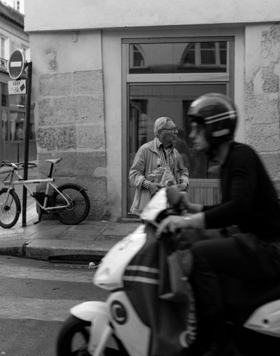 A vertical grayscale shot of a man on a motorbike in Paris, France