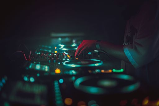 A selective focus of a DJ playing music at a party with cool glowing blue lights in a dark atmosphere