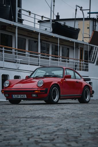 a red Porsche 911 parked in front of a cruise ship at dawn