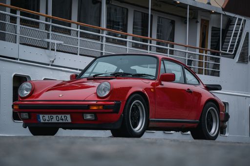 A 1986 red Porsche 911 Carrera parked next to a boat