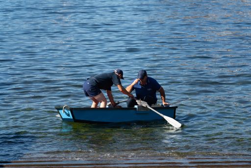 Two men, rowing in a small boat, in shallow water, in Madeira, Portugal, on a sunny  day