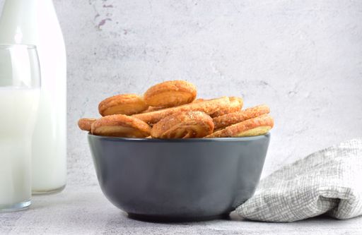 A closeup shot of sweet French pastry, palm leaf shaped, served in a bowl and a glass of milk, with a cloth and a bottle of milk in the background