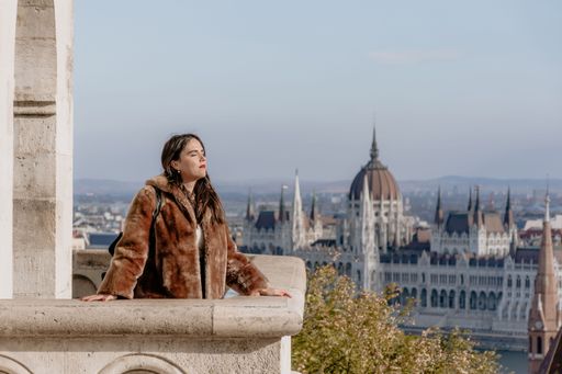 A selective focus of a girl standing on a stone balcony with a Budapest cityscape in the background