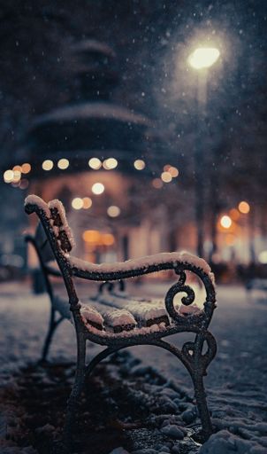 A vertical shot of a snow-covered bench in the park in winter at night