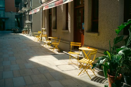 A charming sidewalk cafe with yellow tables and chairs on a sunny narrow street.