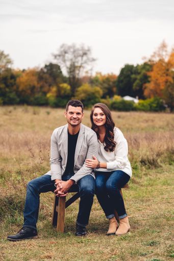 A vertical shot of a happily married couple sitting together on a bench in a sunny field for their portrait