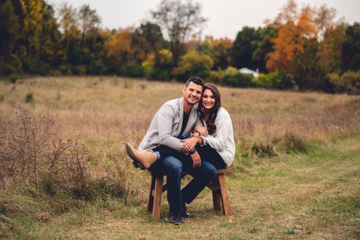 A cute caucasian couple sitting on the bench in the field with lush trees in the background