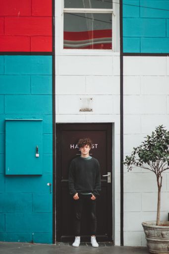 A vertical shot of a South African with curly hair standing in front of the black door