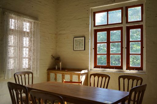 A vintage interior with a red window, a painting in a frame hanging on a wall, and wooden furniture
