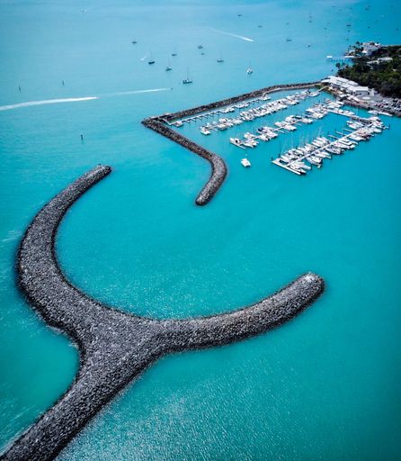 An aerial shot of a rocky line in the middle of an ocean surrounding the boats on the dock