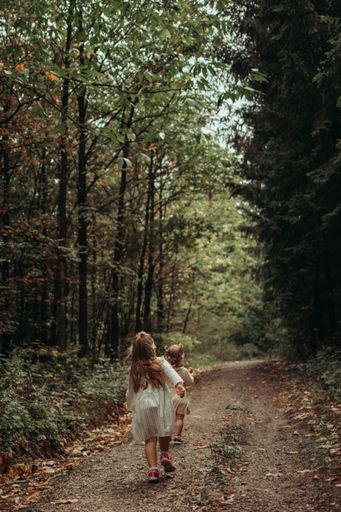 A vertical beautiful shot of a young female child in a dress walking on a forest trail