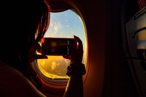 A young female taking a photo of the sunset out the window of an airplane