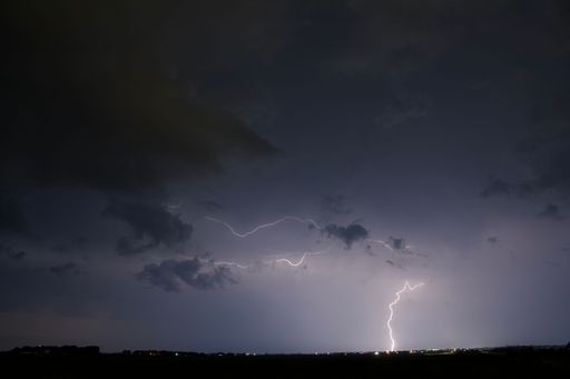 A beam of lightning in a clear night sky strikes a field