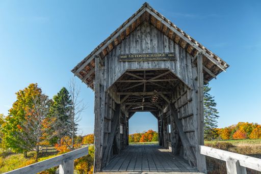 A scenic shot of the wooden AM Foster Bridge surrounded by autumn foliage and blue sky