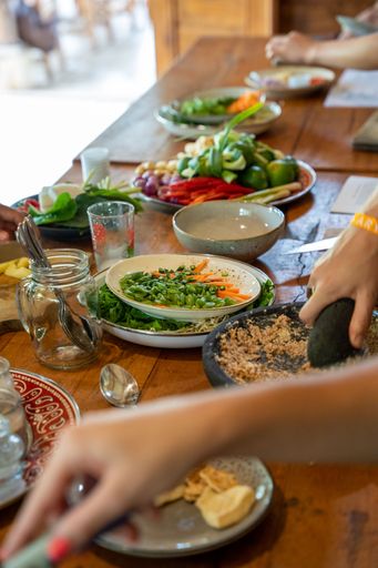 fresh healty organic ingredients on a wooden table at a cooking class in Bali, Indonesia. You see different plates with onions, limes, carottes, salad