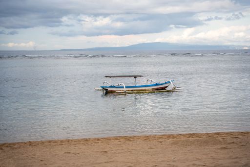 indonesian jukung at the coast of Sanur, Bali with landmarks in the background and sand in the foreground