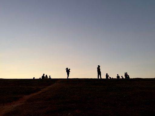 The silhouettes of people standing on the top of small hill during light blue sunset