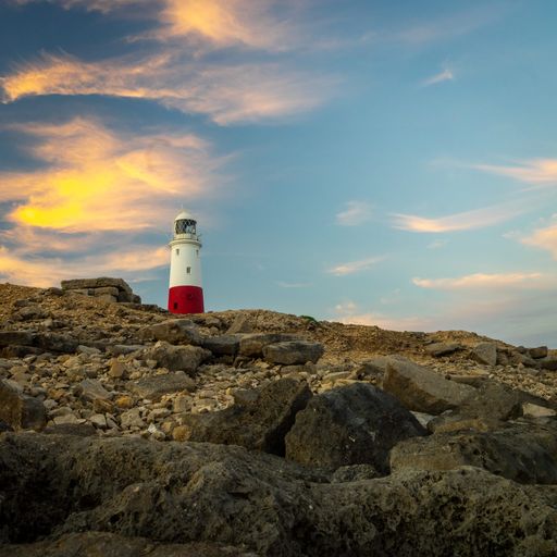 A lighthouse on a rocky coast under a blue cloudy sky