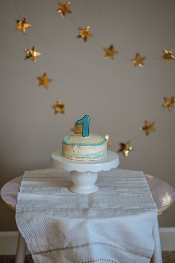 A vertical shot of delicious cake for first birthday with blue candle on table and garland with stars in background