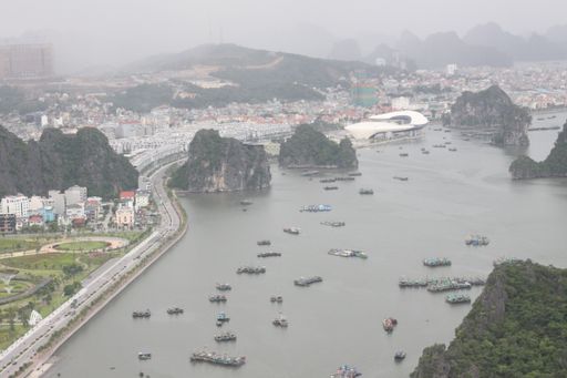 A high angle shot of a sea full of green rock formations and ships in the middle of a city