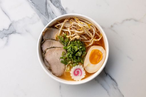 A top view of a delicious ramen bowl with beef and an egg served on the marble table