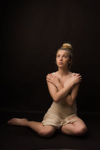 A vertical shot of a woman sitting in a studio and looking up on a black background