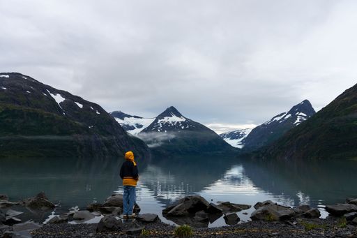 A scenery of a person standing on the shore of the Portage Lake with Bard Peak in the background